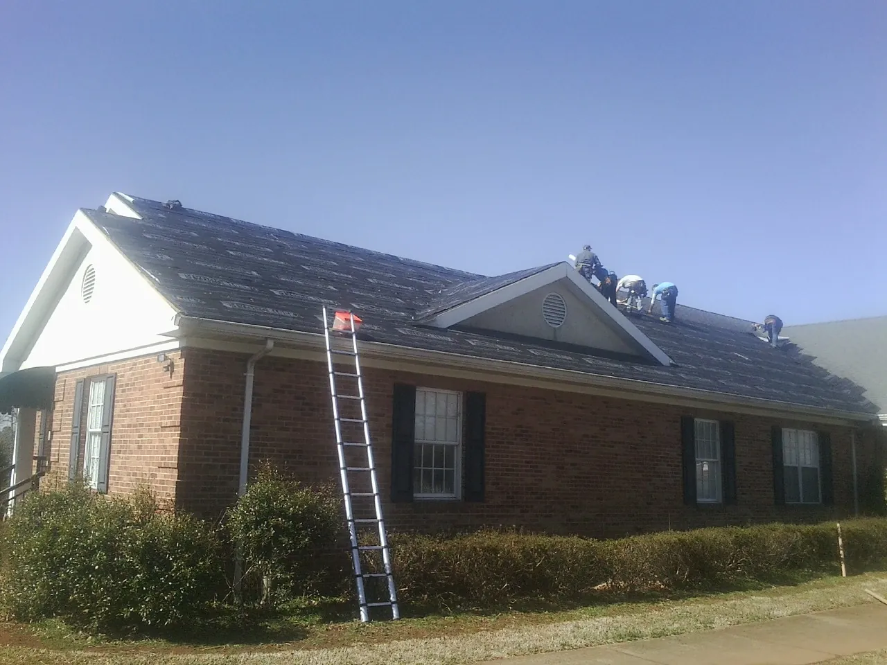 Crew tearing shingles off a brick ranch roof with a ladder set — Metal Roof Repair work by our crew in Longview