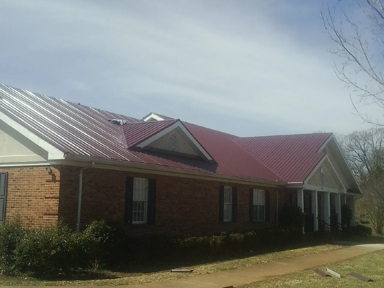 Red metal roof with gabled entries on a long brick building, from a Hail Damage Roof Repair job in Longview
