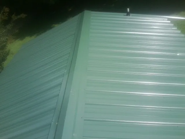 New green metal panels meeting at the ridge of a roof — Flat Roof Repair work by our crew in Longview