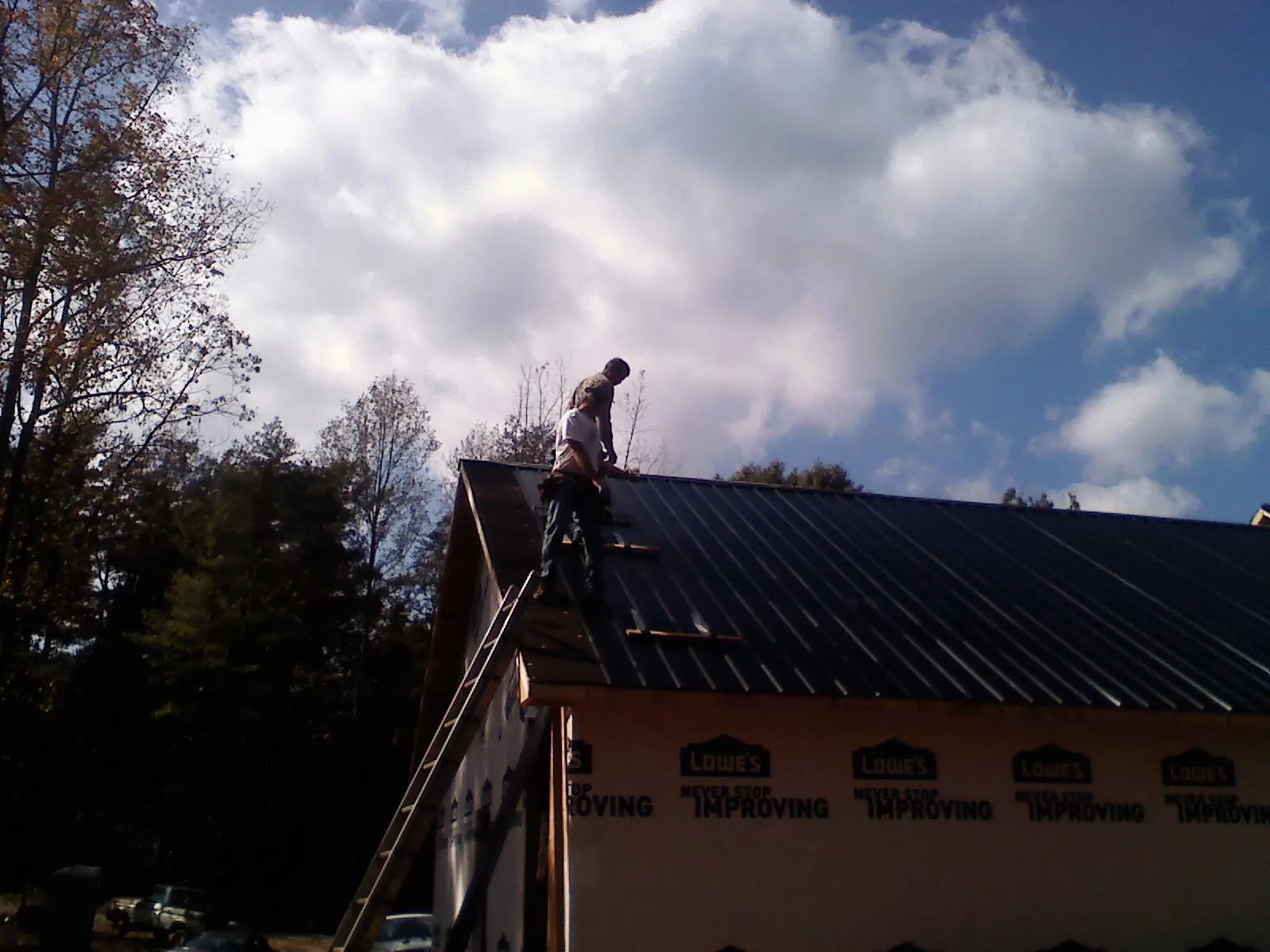 Roofer fastening dark metal panels high against a cloudy sky, from a Roof Inspection job in Longview
